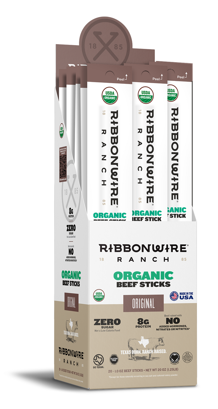 A retail display box of Ribbonwire Ranch Organic Beef Sticks, showing four individual stick packs standing upright inside. The packaging is primarily white and beige with brown accents and green text highlighting the organic beef stick flavor.