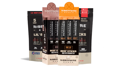 A retail display box filled with Ribbonwire Ranch beef sticks, shown alongside two individual pouches of beef sticks on a clean white background.